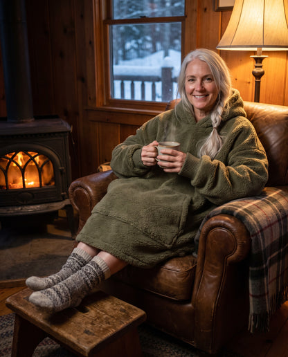 MAPLE hooded wearable blanket in Army Green, in an armchair by the stove
